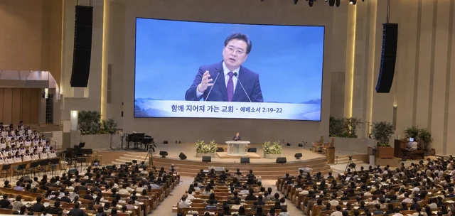 대형 교회 강당 정면 LED 화면에 설교 중인 목회자 실시간 영상과 자막이 표시된 모습