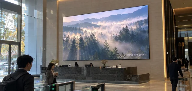 오피스 로비 안내데스크 뒤 LED 미디어월에 숲 영상과 환영 문구가 표시된 모습