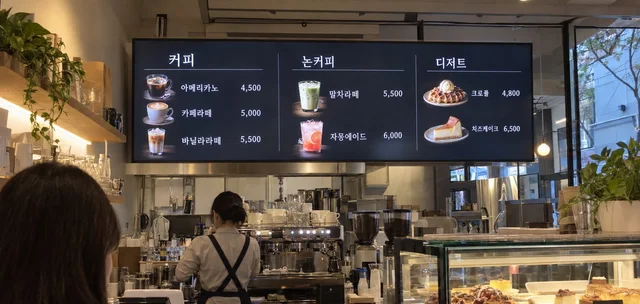 카페 카운터 위 가로형 LED 메뉴보드에 커피와 디저트 메뉴, 가격이 표시된 모습